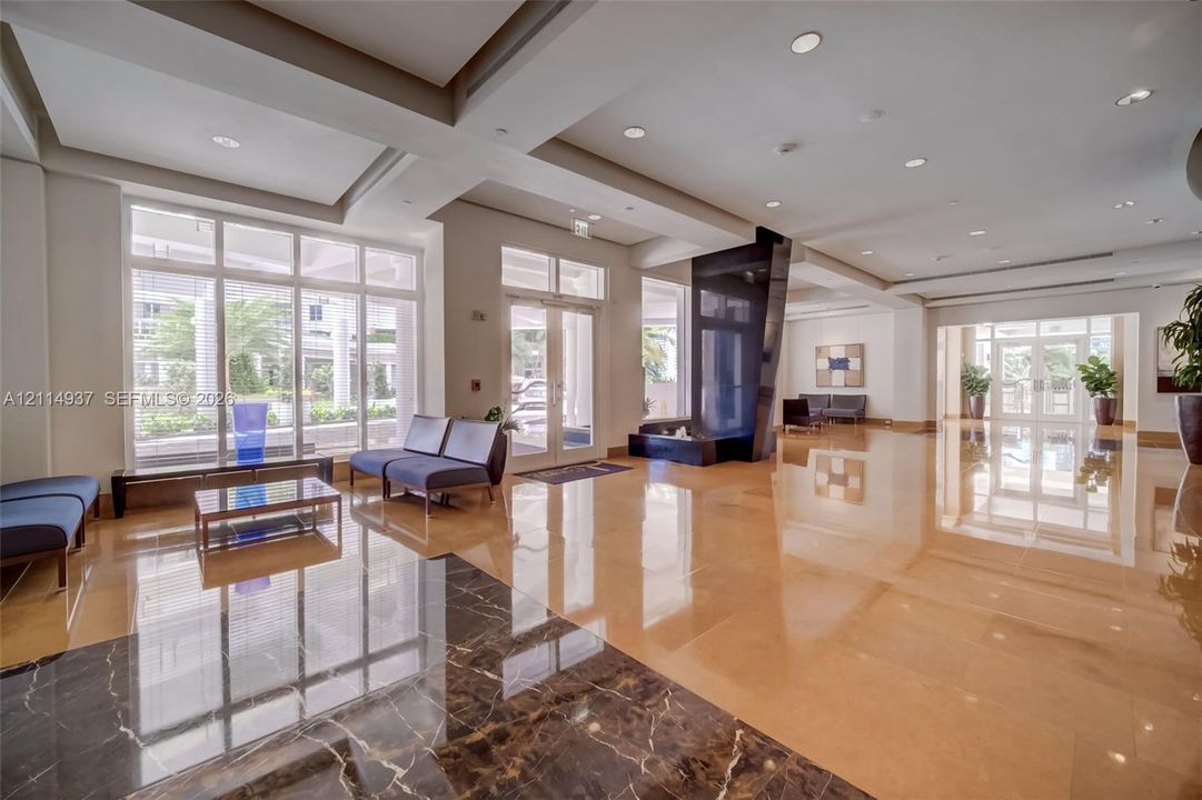 Expansive foyer featuring polished stone flooring, recessed ceiling lighting, full-height windows, a prominent black stone feature wall, and double-door entryway