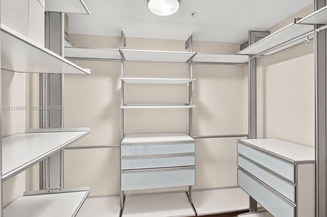 Walk-in closet featuring floor-to-ceiling metal shelving units, adjustable white laminate shelving, and two built-in drawer stacks with white flat-panel faces