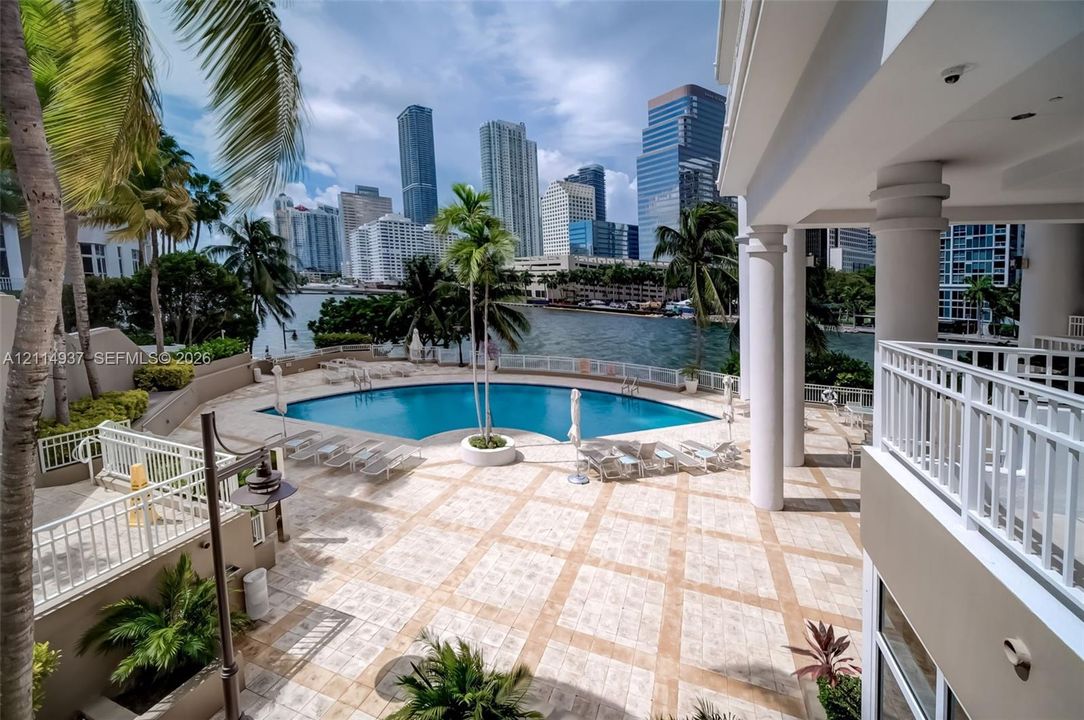 In-ground swimming pool with stone deck, white columned terrace, and waterfront setting