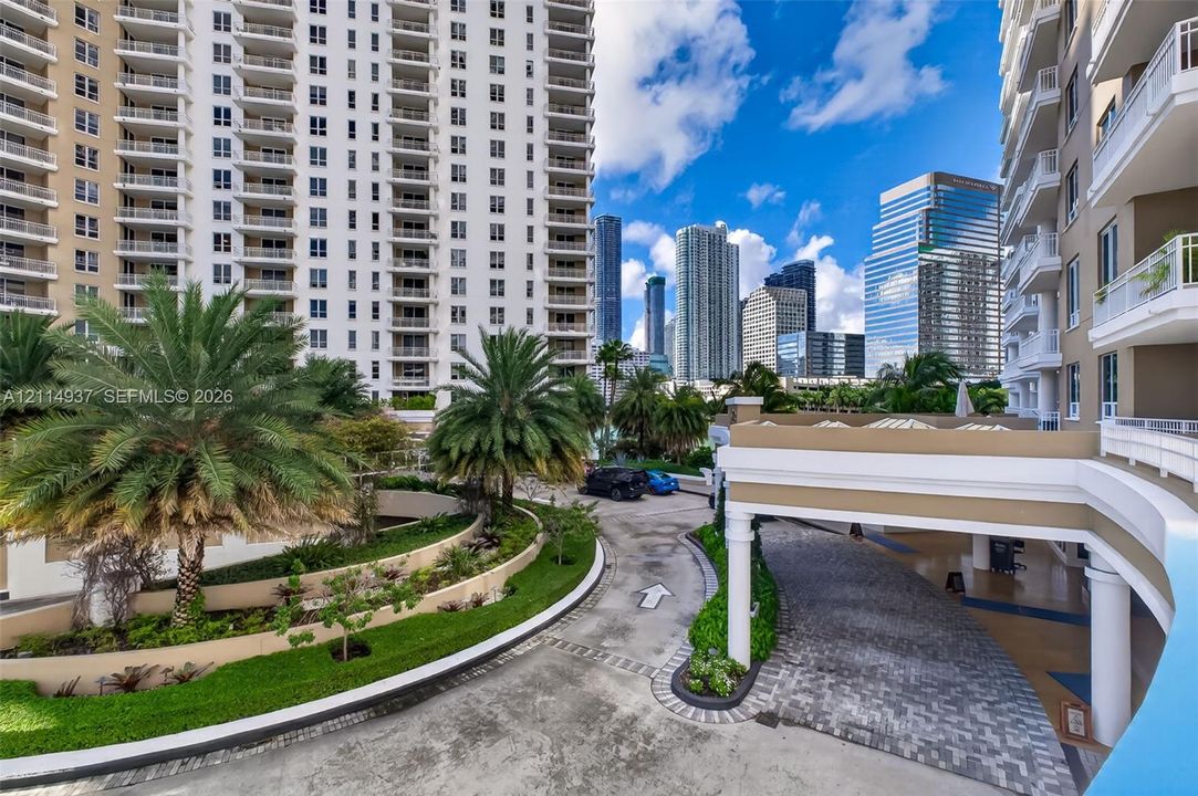 Covered porte-cochère entry with paved drive, terraced landscaping featuring mature palm trees, and multi-story high-rise architecture