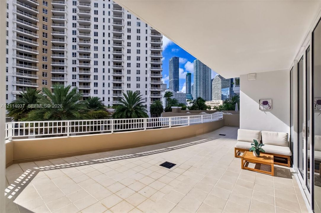 Curved balcony featuring light-colored tile flooring, a white metal railing, and urban skyscraper scenery