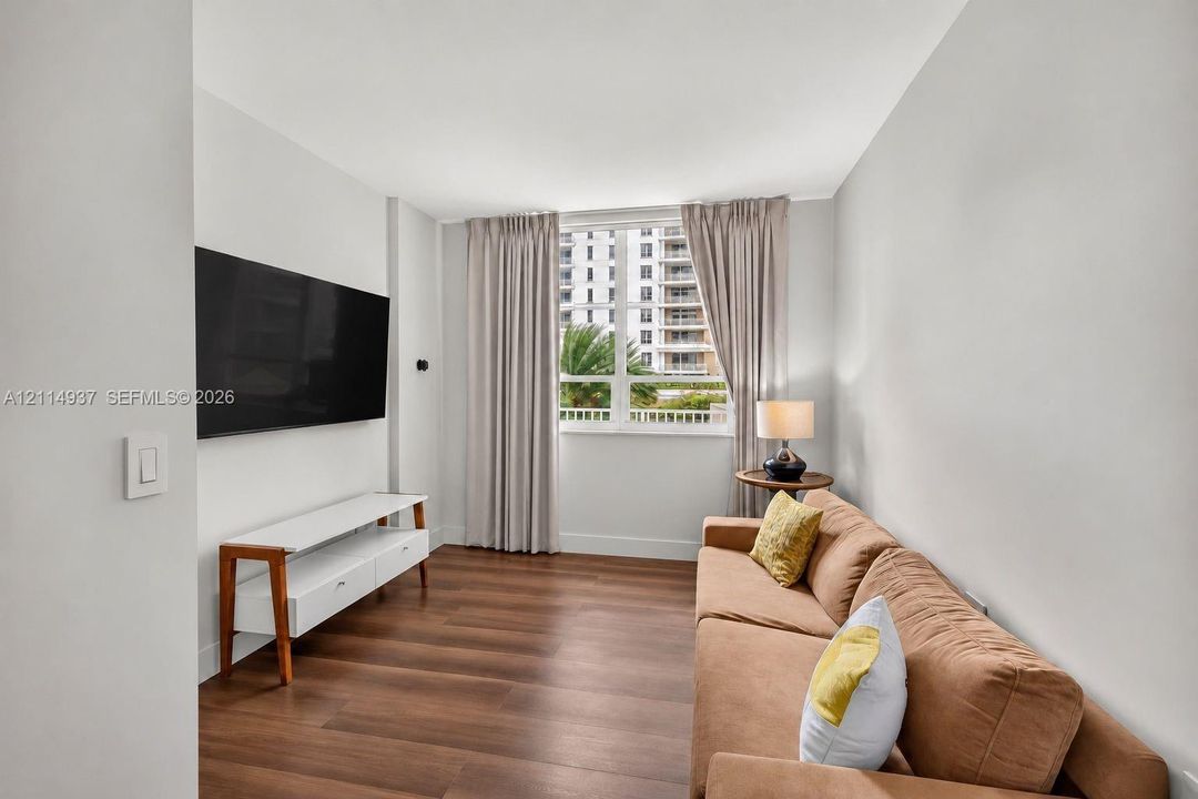 Living area featuring wood-finish flooring, neutral wall tones, and a large window with white muntins