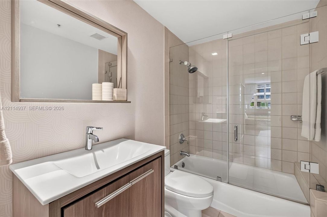Wall-mounted wood-finish vanity with an integrated basin, frameless glass shower enclosure, bathtub with polished chrome fixtures, and a framed mirror