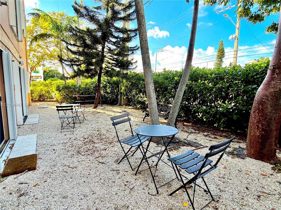 Outdoor space featuring crushed stone hardscaping, mature trees, and perimeter privacy hedging
