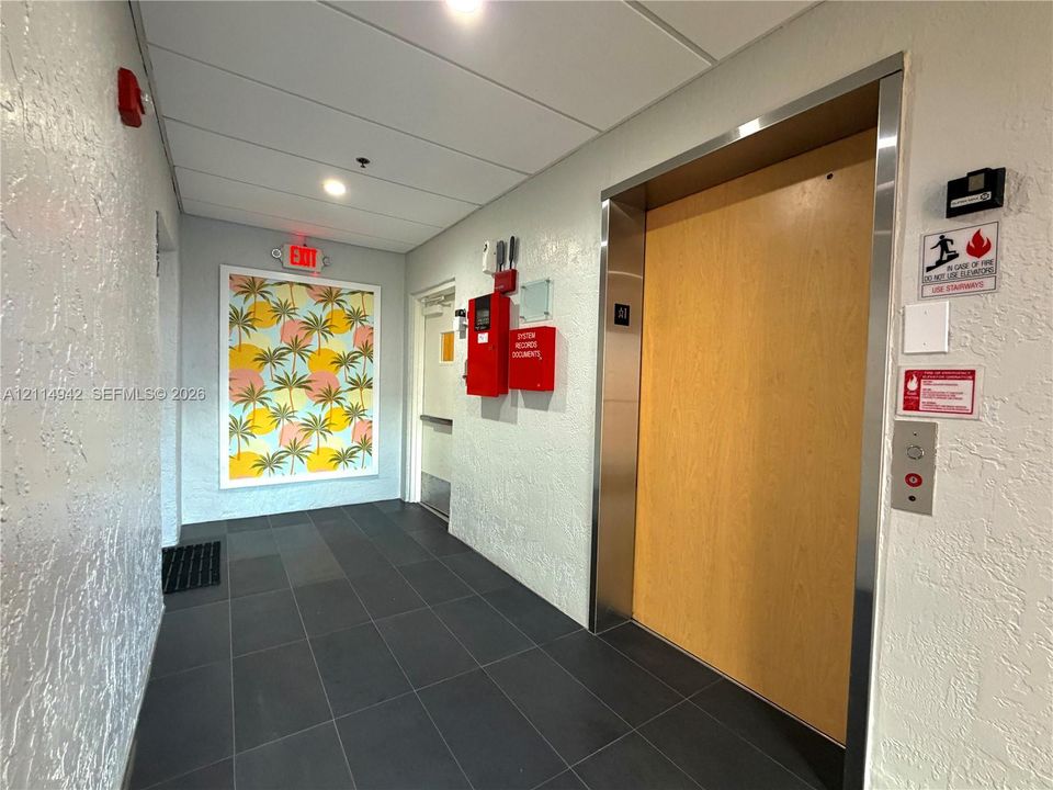 Elevator lobby featuring a stainless steel frame, wood-veneer door, large-format grey tile flooring, and textured wall finish
