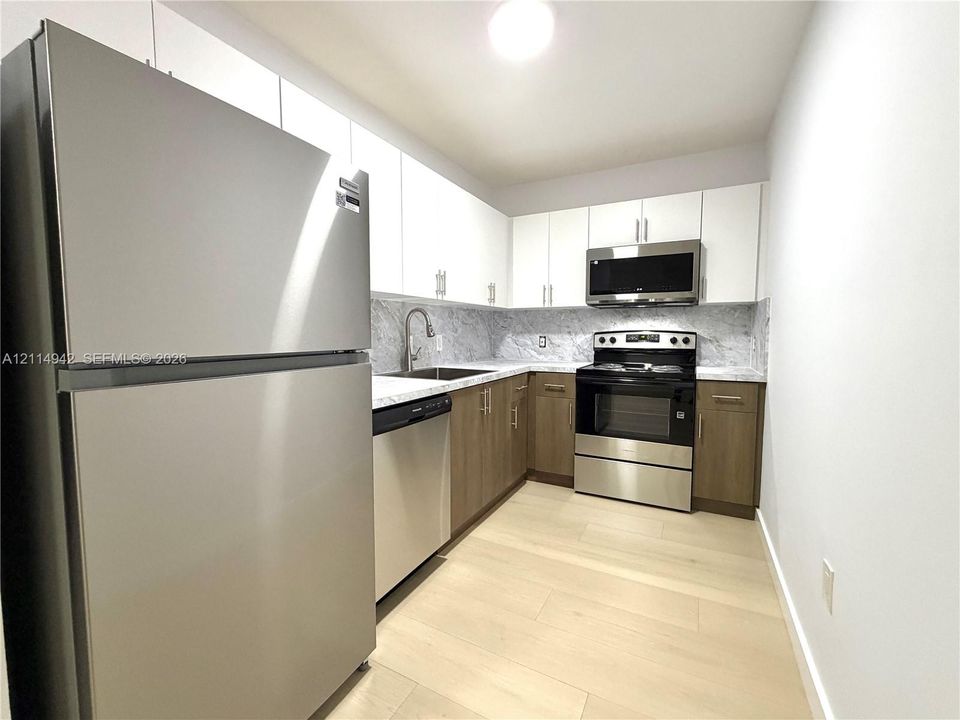 Kitchen featuring stainless steel appliances, dual-tone cabinetry, stone-patterned countertops, a high-arc faucet, and light wood-finish flooring