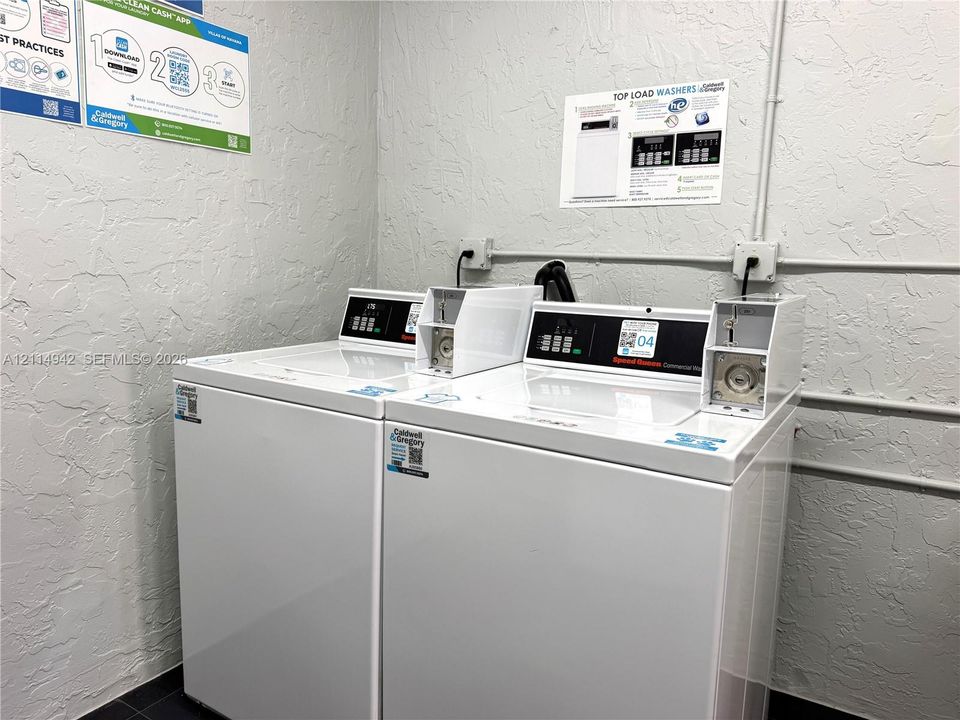 Laundry room featuring dual commercial top-load washers with integrated coin-operated payment modules and textured wall finish