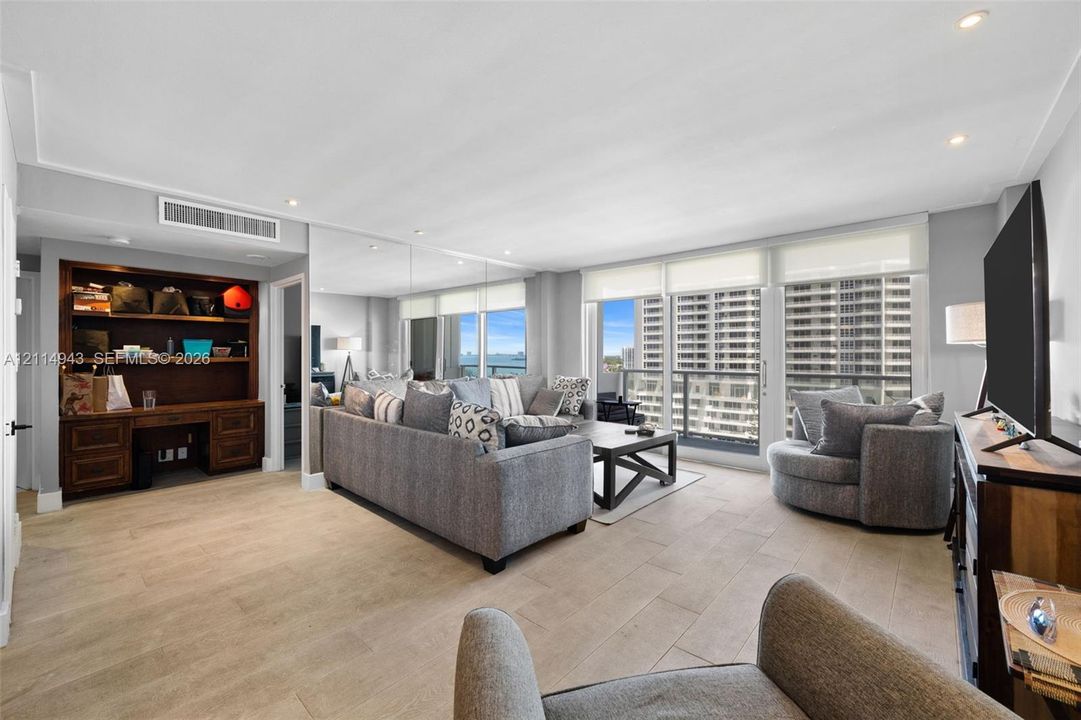 Open living space featuring wood-finish flooring, recessed lighting, built-in dark wood cabinetry, floor-to-ceiling mirror panels, and sliding glass doors