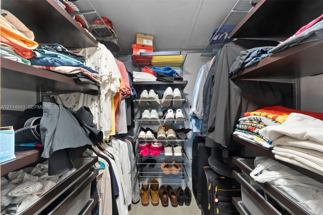 Walk-in storage space featuring multi-level dark wood-finish shelving, overhead wire racking, and integrated central shoe shelving units