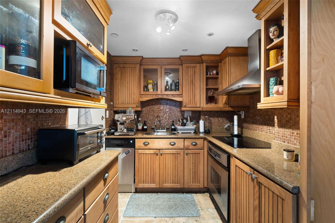 Kitchen featuring custom beadboard-style wood cabinetry, stone countertops, a mosaic tile backsplash, stainless steel appliances, and glass-paneled upper cabinets
