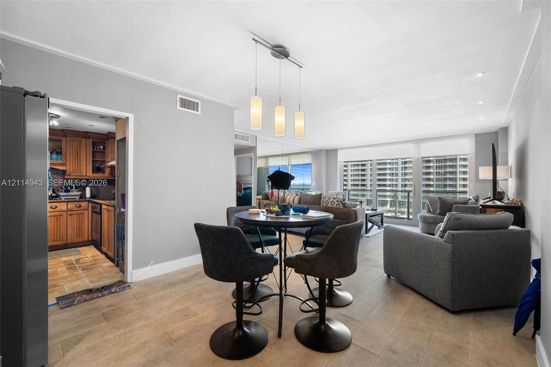 Open-concept living space featuring wood-finish flooring, recessed lighting, a modern three-pendant chandelier, and expansive floor-to-ceiling windows