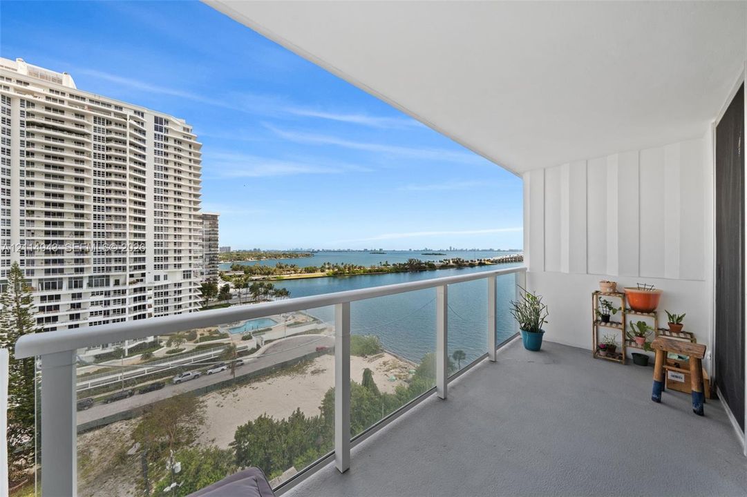 Covered balcony featuring a glass-panel railing and concrete flooring, overlooking a coastal landscape