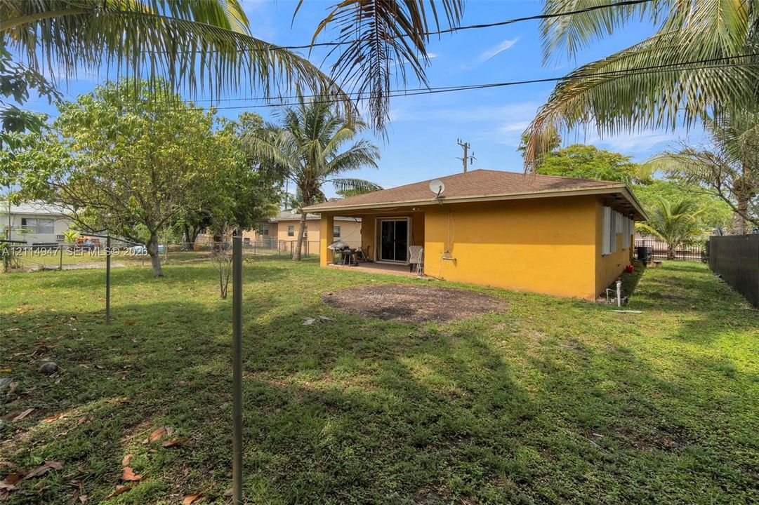 Rear exterior featuring a covered patio, expansive lawn, mature palms, and metal perimeter fencing