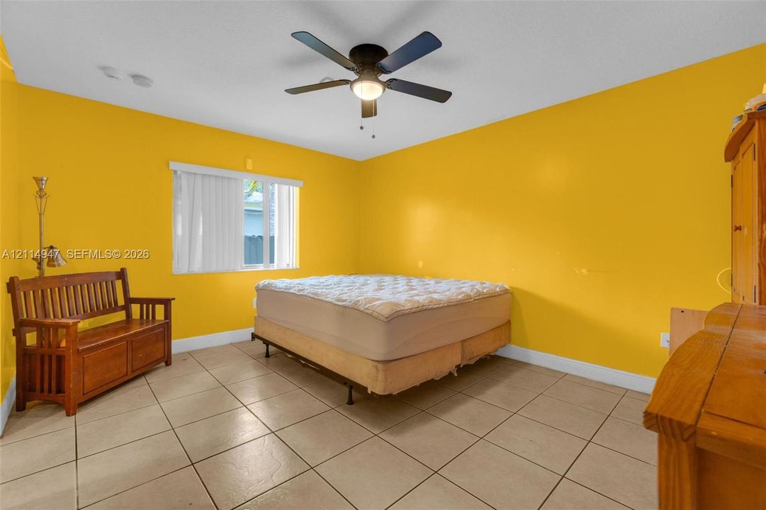 Spacious room featuring neutral ceramic tile flooring, a central ceiling fan with integrated lighting, and vertical window blinds