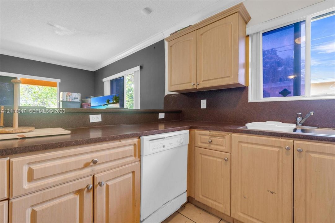 Kitchen featuring light-finish wood cabinetry, solid-surface countertops, integrated white dishwasher, and sliding windows