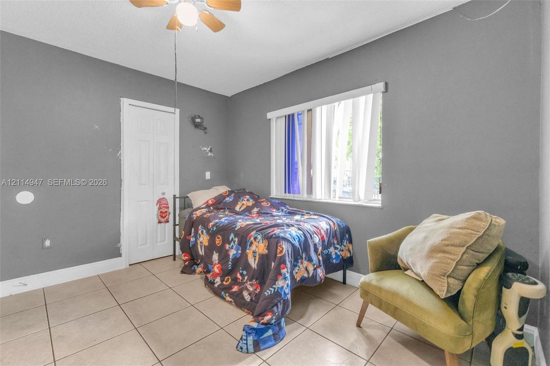 Room featuring large-format neutral floor tile, a central ceiling fan with integrated lighting, and a white six-panel door