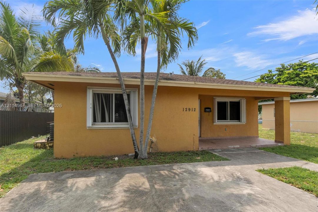 Stucco exterior featuring a covered front porch, concrete driveway, and mature palm trees