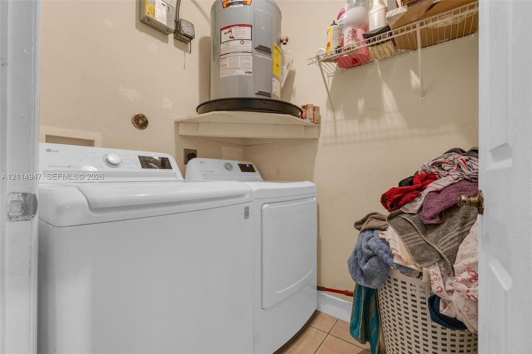 Dedicated utility space featuring a cylindrical water heater, mounted wire shelving, and tile flooring