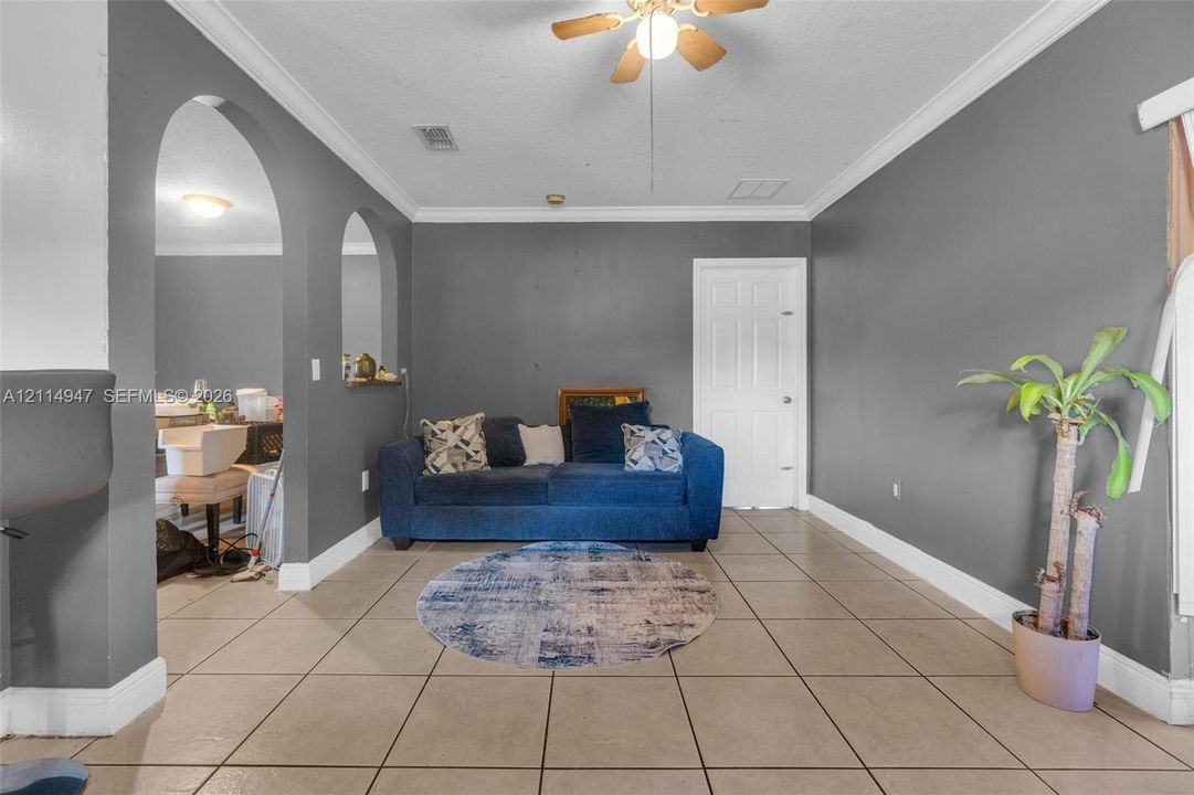 Ceramic tile flooring, arched wall cutouts, crown molding, and a central ceiling fan
