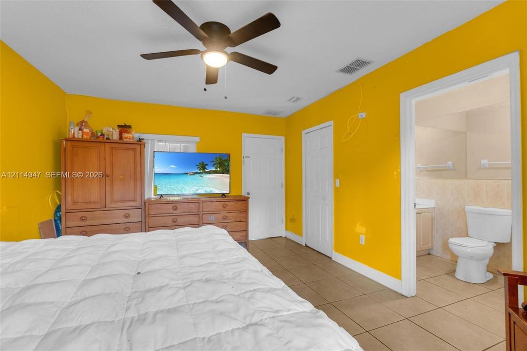 Room featuring tile flooring, ceiling fan with integrated lighting, and multiple interior doors, including access to a bathroom equipped with a toilet and vanity