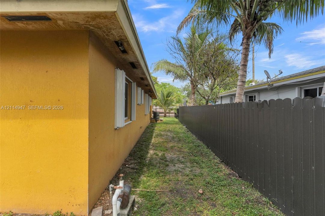Side exterior area featuring a stucco wall, mounted storm shutters, and a vertical wood-style privacy fence