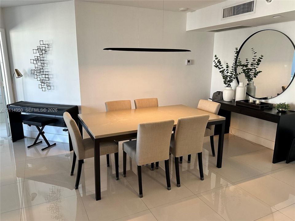Open-concept dining area featuring large-format tile flooring, a minimalist linear pendant light, and a circular wall-mounted mirror