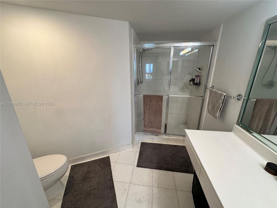 Bathroom featuring a shower stall with a glass enclosure, tile flooring, vanity with a solid-surface countertop, and a wall-mounted mirror