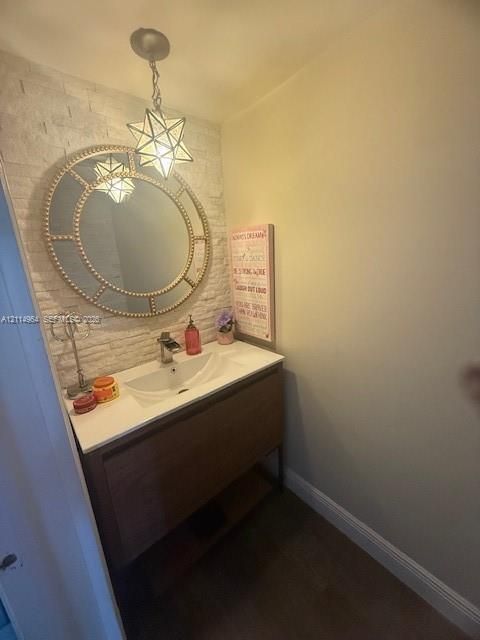 Vanity featuring a wood-finish cabinet with an integrated white sink, textured stone accent wall, decorative circular wall-mounted mirror, and geometric pendant lighting