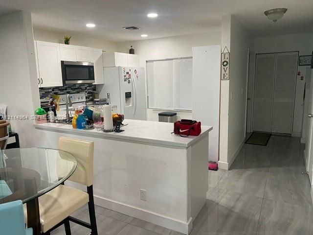Kitchen featuring white cabinetry, a peninsula with a solid-surface countertop, tile backsplash, recessed lighting, and large-format tile flooring