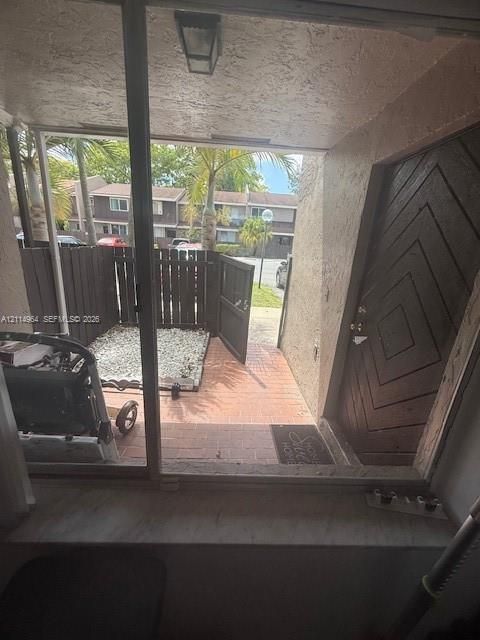 Entryway featuring a decorative dark wood-paneled door, terracotta-style paved patio, stone-covered ground area, and a wood privacy fence