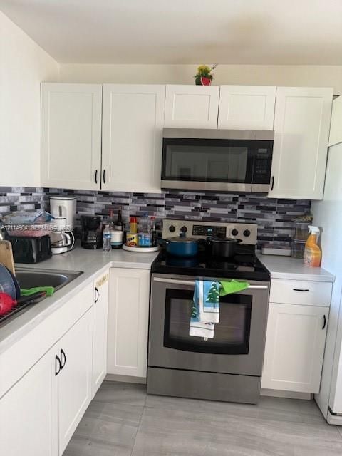 Kitchen featuring white shaker-style cabinetry, stainless steel appliances, multi-tonal linear tile backsplash, solid-surface countertops, and large-format tile flooring