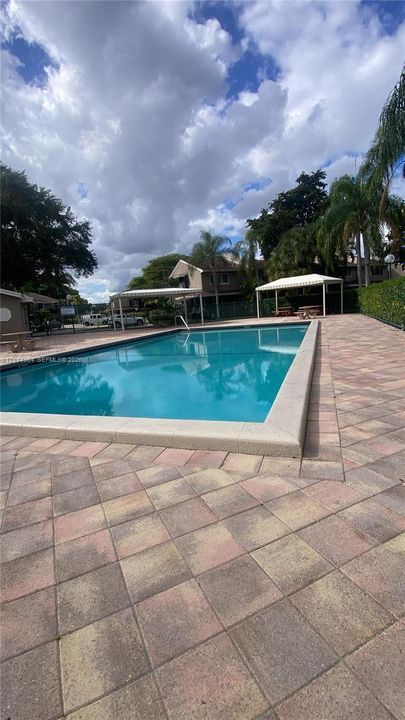 Rectangular swimming pool featuring a concrete coping border, paver stone pool deck, and two covered cabanas