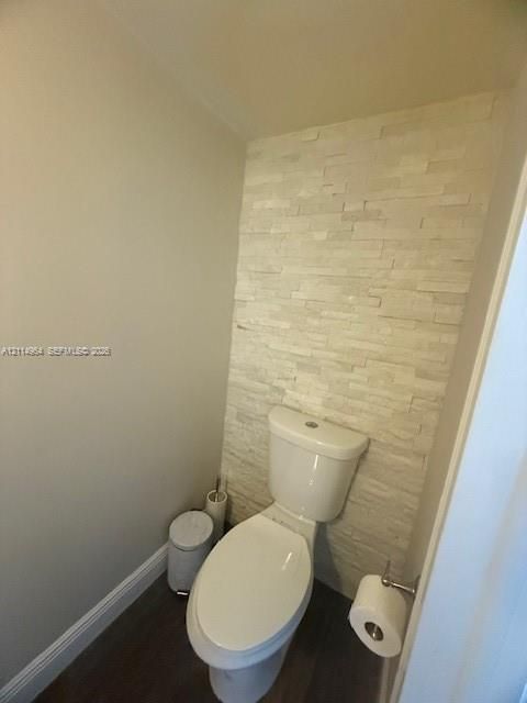 Stacked stone wall accent, white porcelain toilet, and dark wood-finish flooring