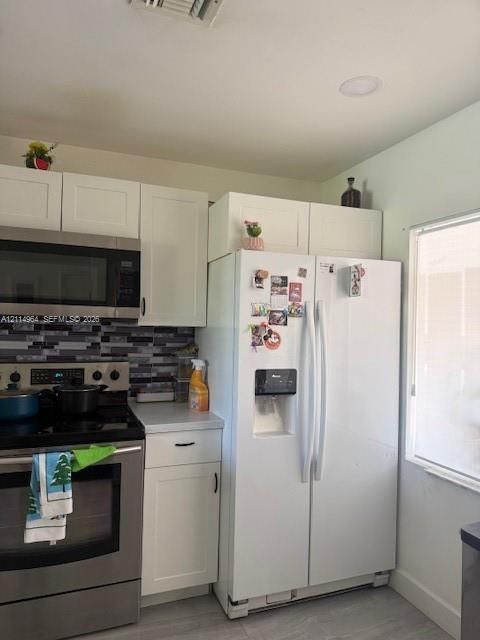 Kitchen featuring white shaker-style cabinetry, mosaic tile backsplash, stainless steel microwave, and wood-finish flooring