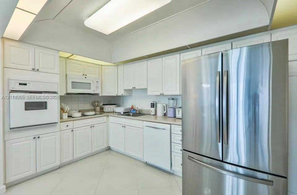 Kitchen featuring white cabinetry, integrated wall oven, stainless steel refrigerator, neutral solid-surface countertops, and tiled flooring