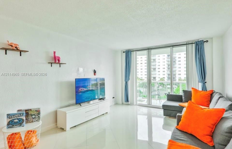 Living space featuring polished tile flooring, white walls, and sliding glass doors with access to an exterior balcony