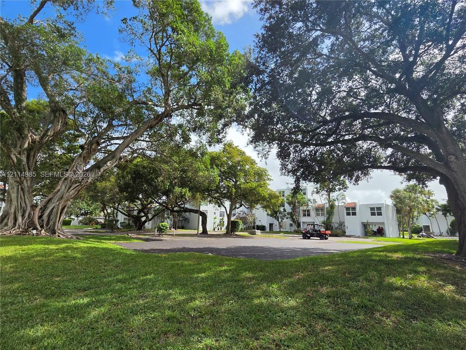 Expansive grounds featuring mature trees and a manicured lawn surrounding a paved parking area