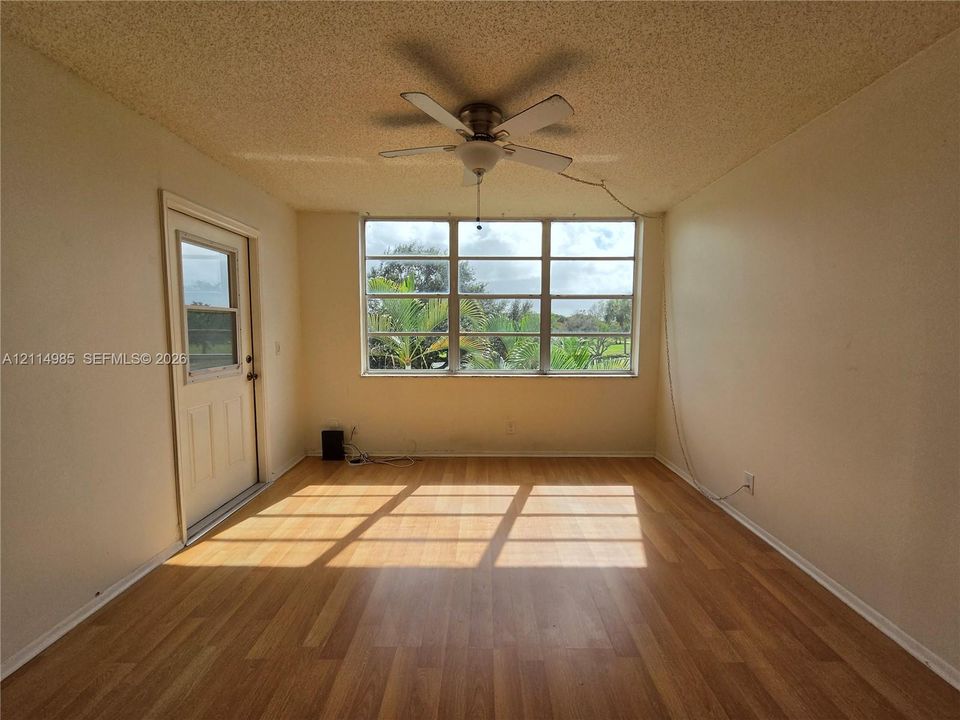 Room featuring wood-finish flooring, a multi-pane window, a ceiling fan with integrated lighting, and an exterior door