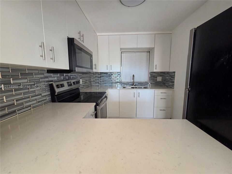 Kitchen featuring white flat-panel cabinetry, light-toned stone-surface countertops, subway tile backsplash, stainless steel appliances, and a double-basin undermount sink