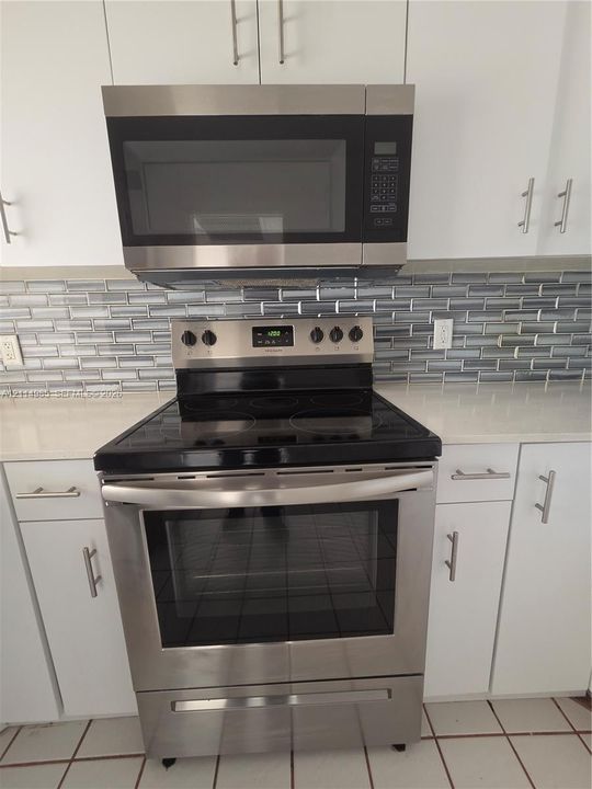 Stainless steel electric range and microwave, white cabinetry, light-toned countertop, and glass tile backsplash