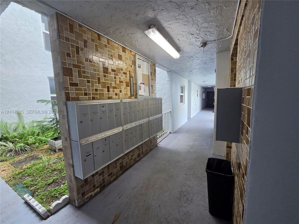 Covered outdoor corridor featuring textured tile wall cladding, integrated stainless steel mailbox bank, and linear overhead lighting