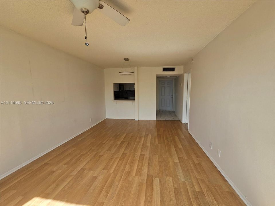 Open-concept room featuring wood-finish flooring, a ceiling fan, and a pass-through opening to the interior space