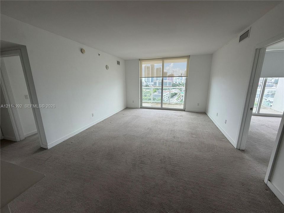 Open interior space featuring neutral carpeting, white walls, and large sliding glass doors accessing a balcony