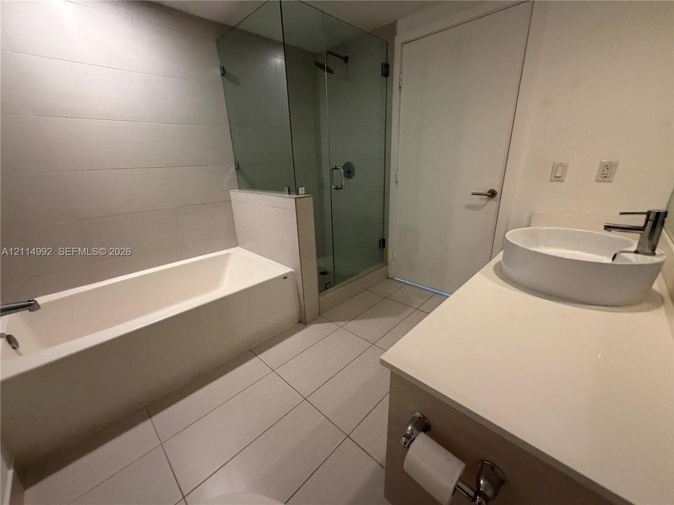 Bathroom featuring a soaking tub, glass-enclosed shower, large-format tile flooring, and a vanity with a circular vessel sink and countertop