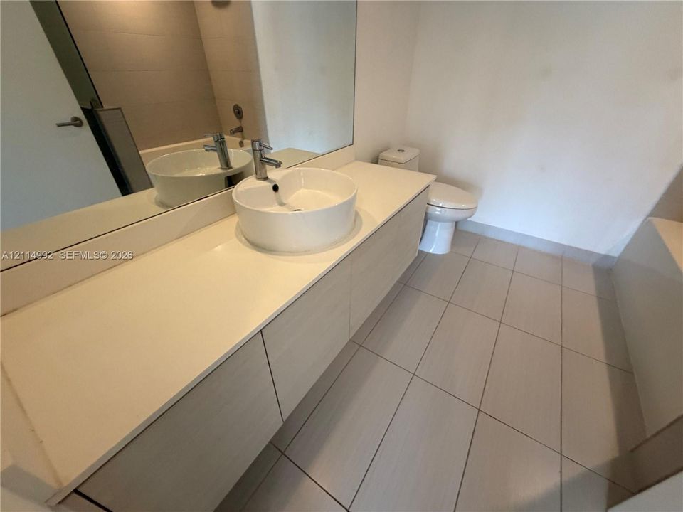 Floating vanity featuring a light-toned wood-finish cabinetry, a round vessel sink, a solid-surface countertop, a large wall-mounted mirror, and tile flooring