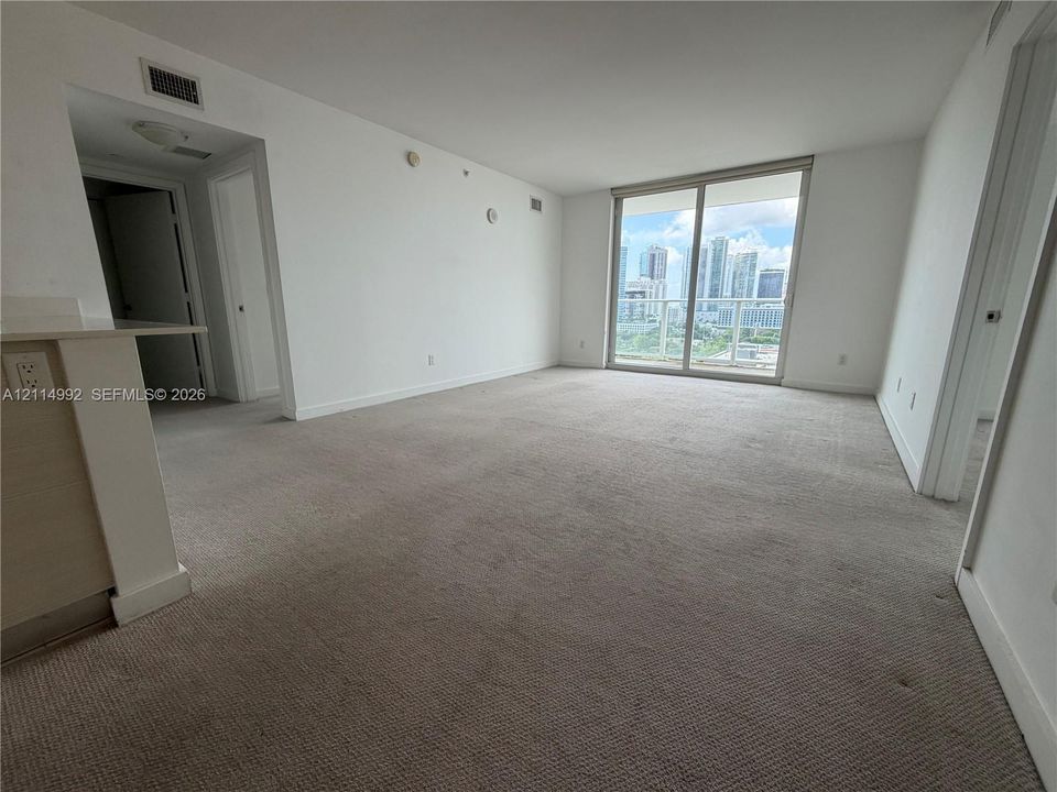 Open interior space featuring wall-to-wall carpeting, expansive glass sliding doors, and a built-in kitchen peninsula with a stone-surface countertop