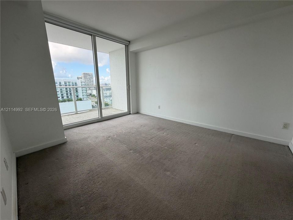 Floor-to-ceiling glass sliding doors, carpeted flooring, and a private balcony with a glass railing