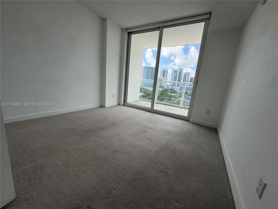 Neutral-toned wall-to-wall carpeting and floor-to-ceiling sliding glass doors opening to a private balcony