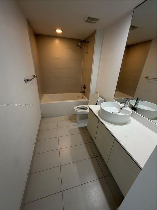 Bathroom featuring a vessel sink atop a solid-surface vanity, full-width mirror, tile flooring, and a bathtub with tile surround