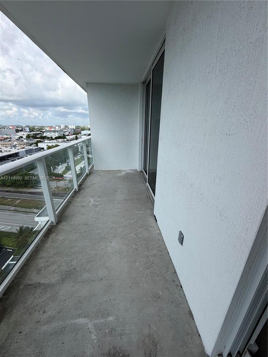 Private balcony featuring a concrete floor, textured stucco wall, and glass-paneled railing